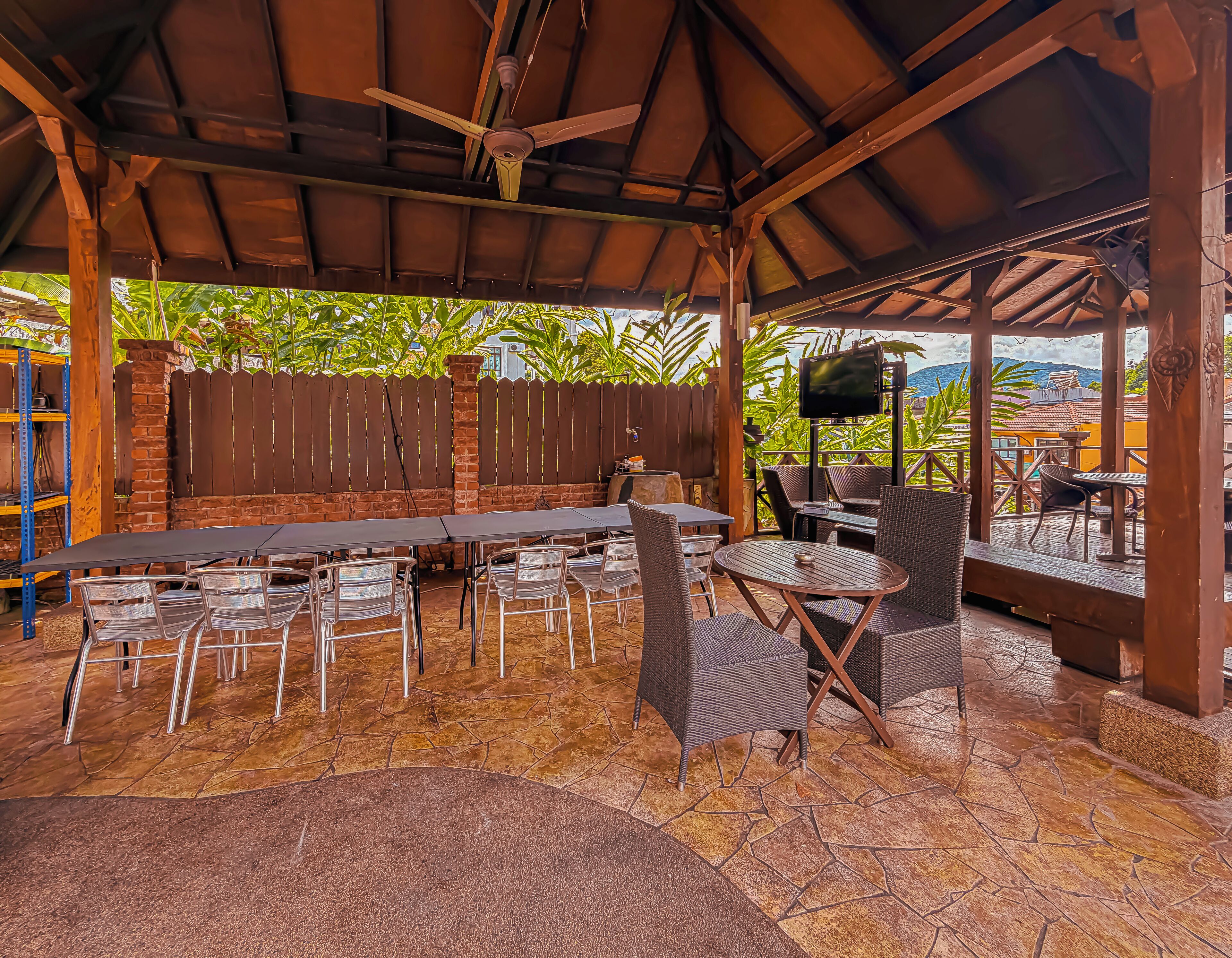 An outdoor patio with a long table and chairs, a ceiling fan, and a TV screen.