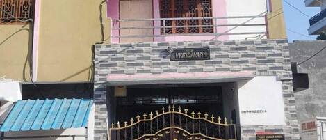 Egy többemeletes épület, amelyen a „Hotel Vrindavan Inn” feliratú tábla látható, és amelyet egy kapuval elzárt bejárat vezet be.