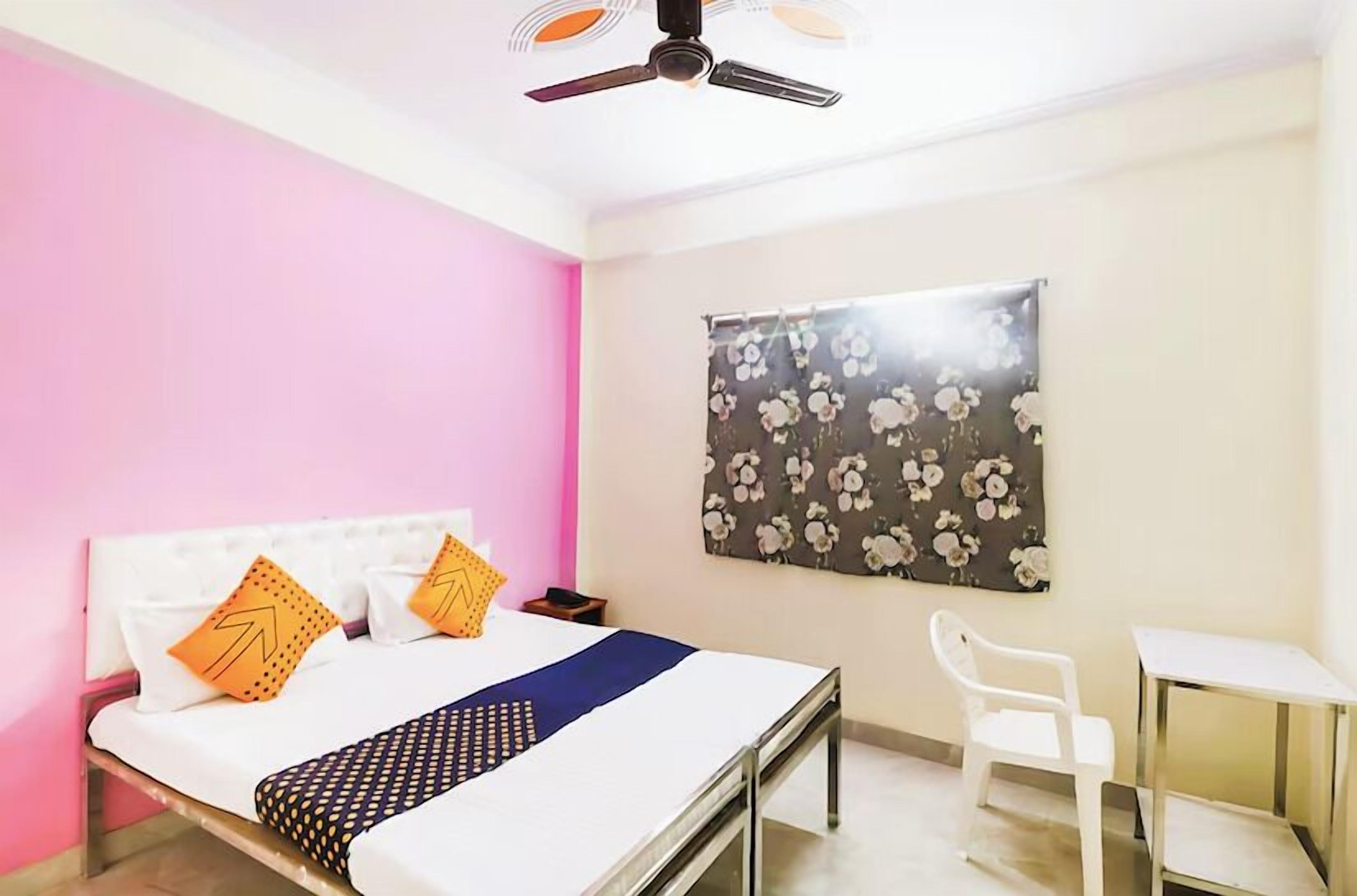 Une chambre à coucher comprenant un lit, un bureau, une chaise, un ventilateur de plafond et une décoration murale à motifs floraux.
