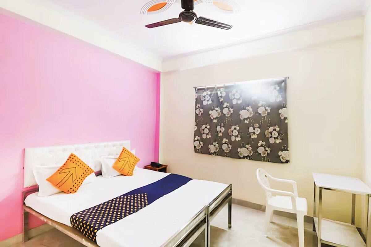 A bedroom with a bed, a desk, a chair, a ceiling fan, and a floral-patterned wall hanging.