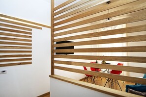 Una habitación con un separador de madera con listones, una zona de comedor con sillas rojas y un enchufe visible en la pared.