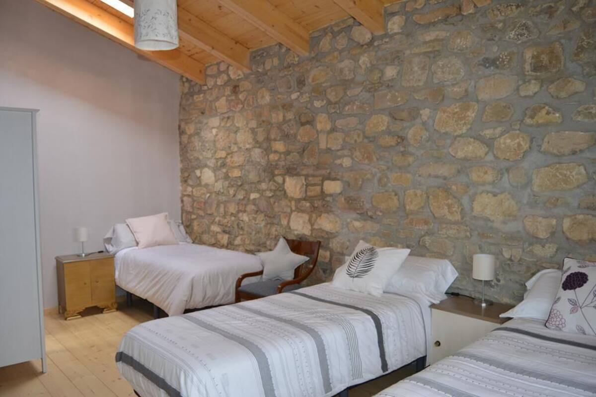 Quarto com duas camas, parede de pedra, vigas de madeira e mesa de cabeceira com abajur.