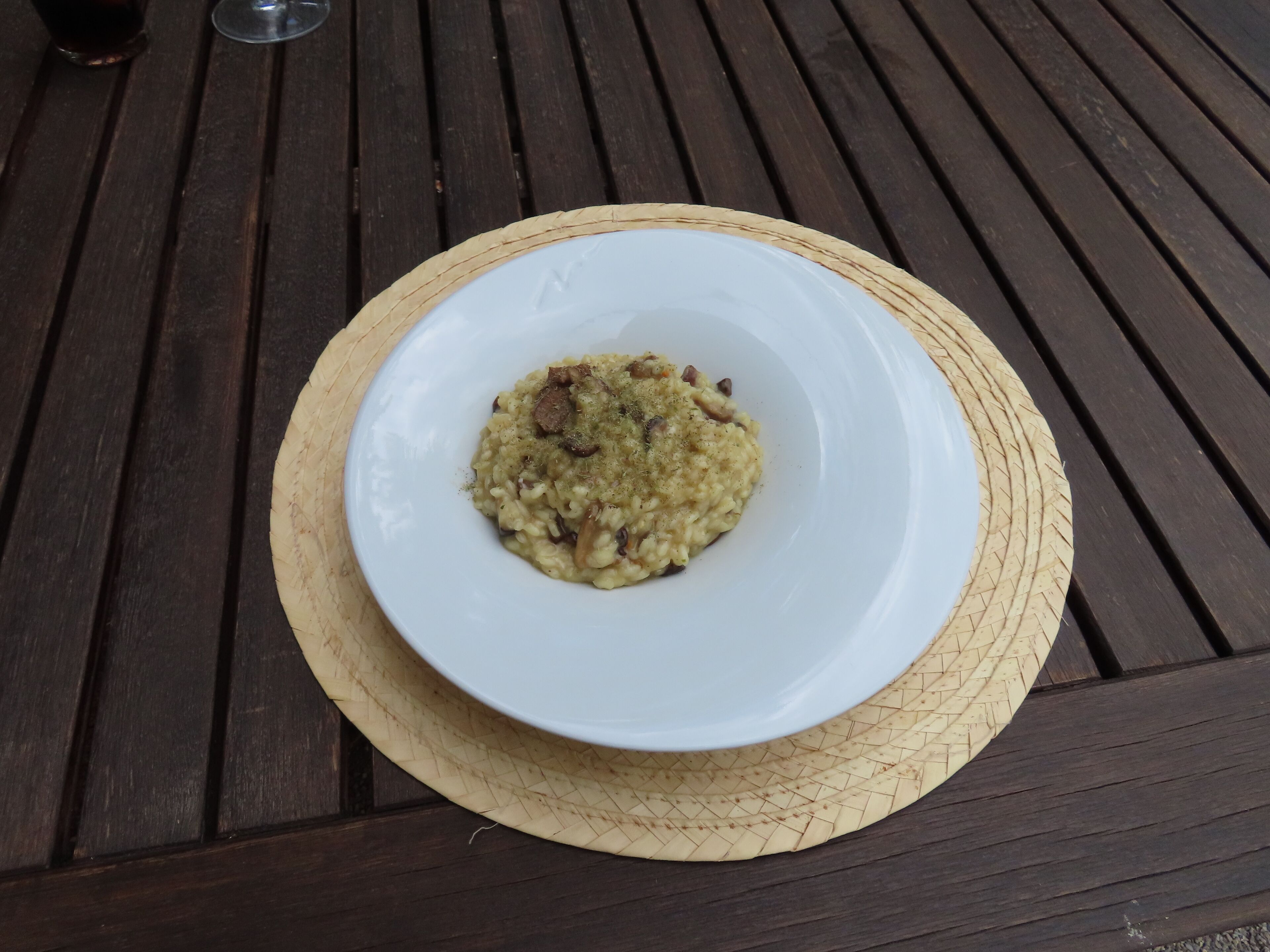 A white plate of risotto with mushrooms on a wooden table.
