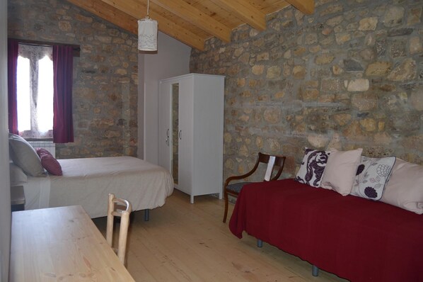 Une pièce avec un mur en pierre, deux lits, une table en bois et une armoire.