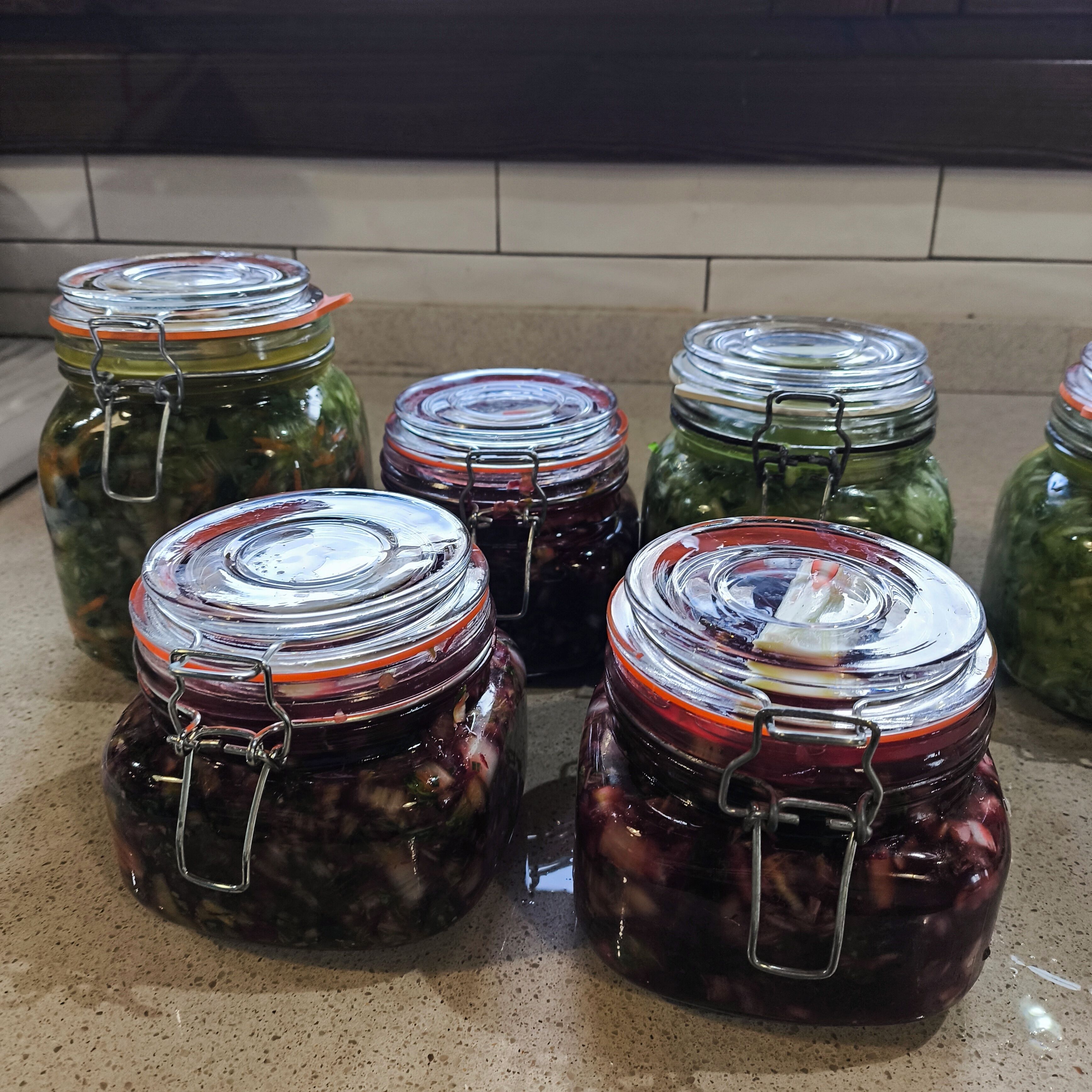 Several glass jars with metal clasps, likely containing preserved foods, arranged on a kitchen countertop.
