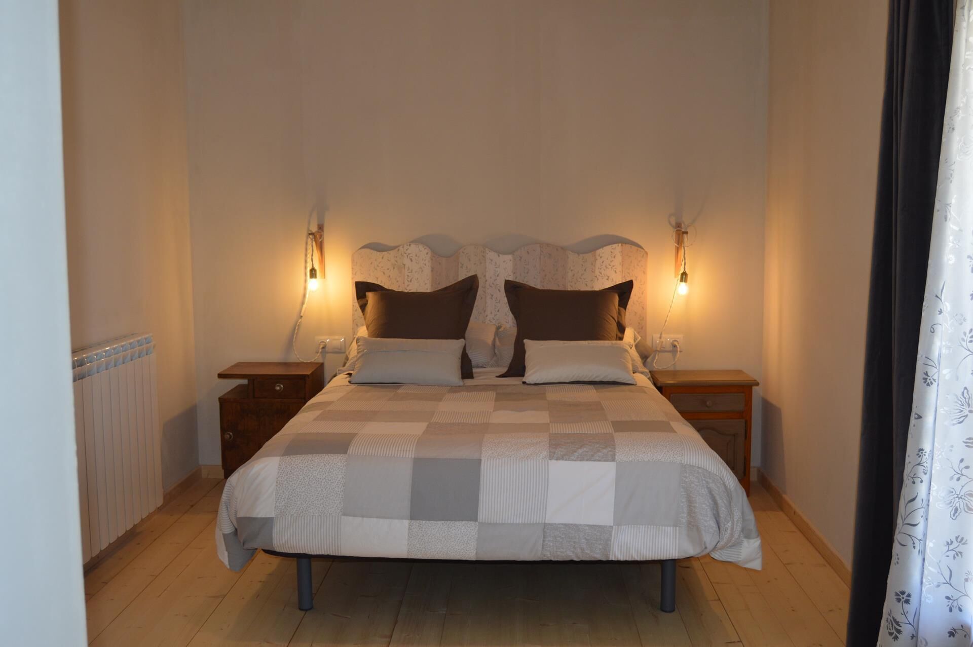 A bedroom with a large bed, two bedside tables, and two wall-mounted lamps.