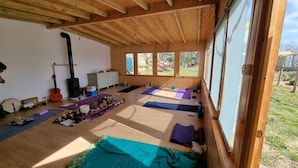A spacious room with wooden beams, large windows, yoga mats, a guitar, a stove, and a cabinet. - Lo Cel De Tolo (Gavet de la Conca)