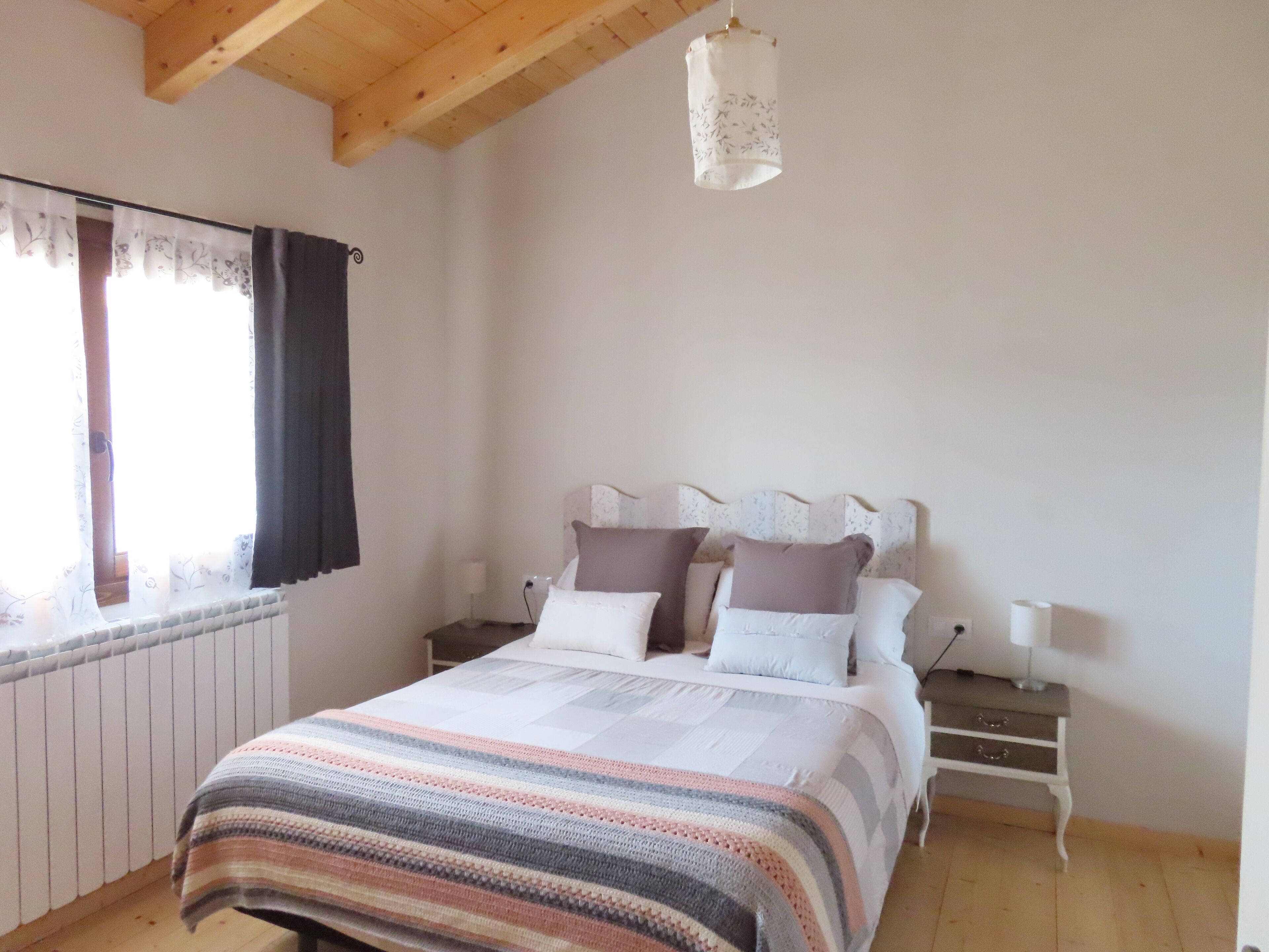A bedroom with a bed, nightstands, a hanging light fixture, and a window with curtains.