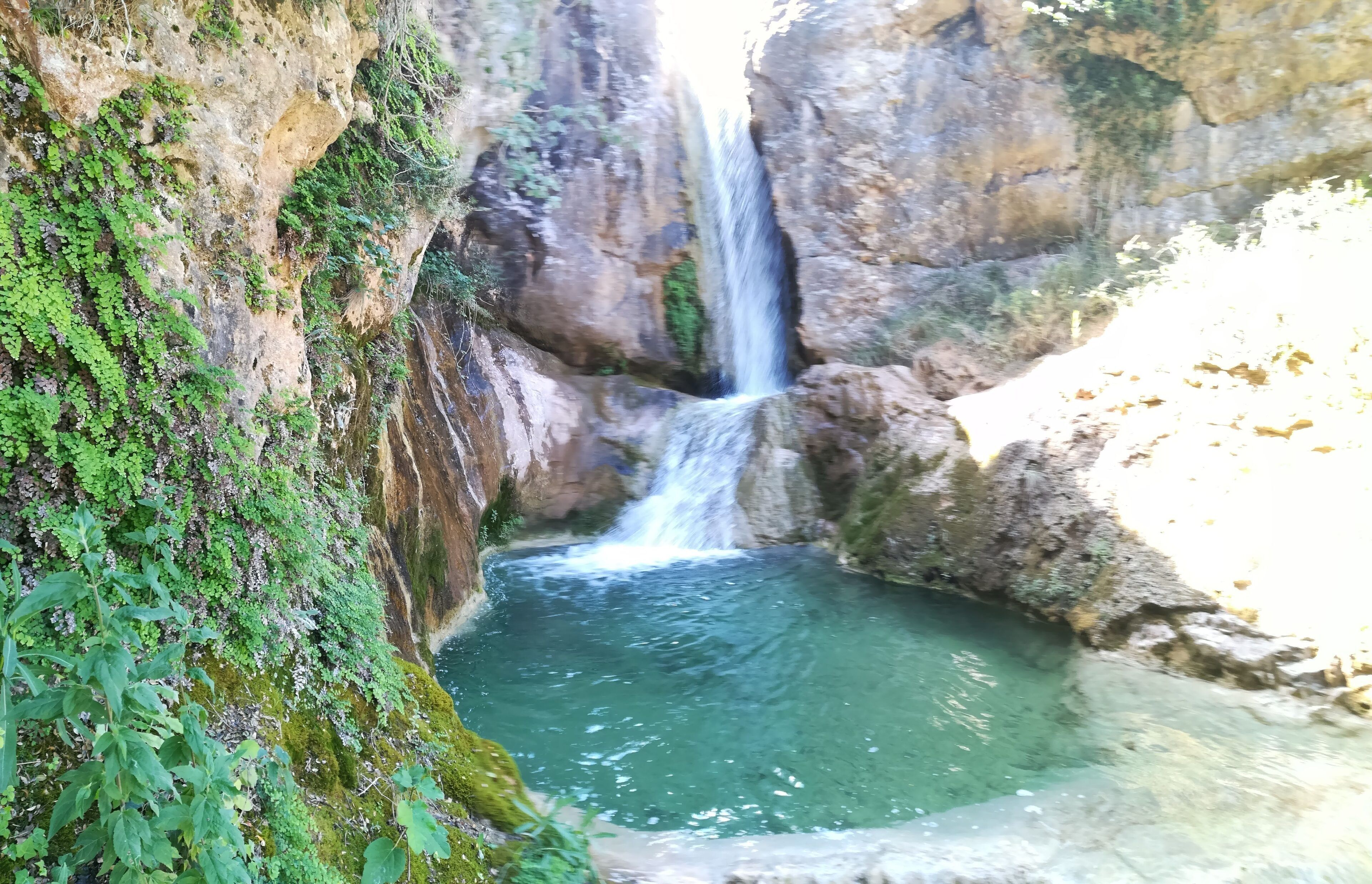 A waterfall cascading into a clear pool surrounded by rocky cliffs.
