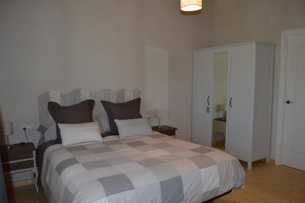Quarto com cama, mesas de cabeceira, guarda-roupa e espelho.