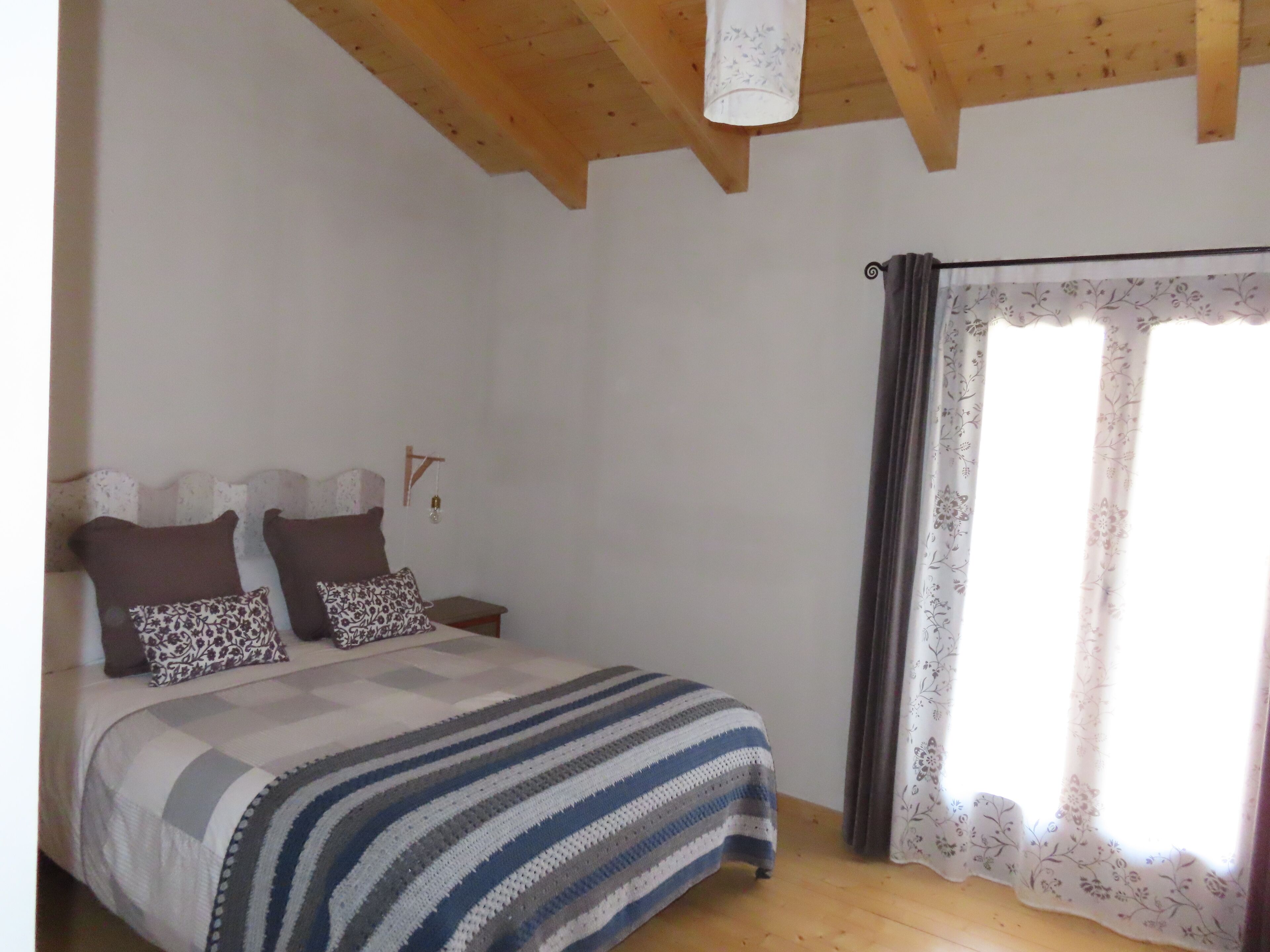A bedroom with a bed, a nightstand, a hanging light fixture, and a window with curtains.