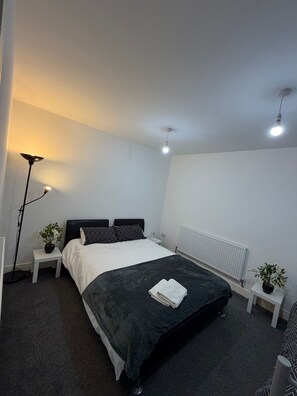 Ein Schlafzimmer mit einem Bett, zwei Nachttischen, einer Stehlampe, einem Heizkörper und einem Blumentopf.