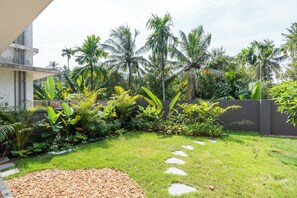 Ein gepflegter Garten mit verschiedenen tropischen Pflanzen und Palmen, einem Kiesweg und einem modernen Gebäude mit flachem Dach.
