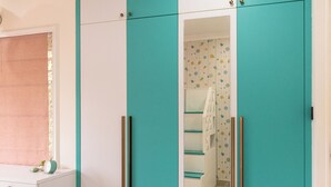 A room with teal and white wardrobe, a small white desk, and a colorful rug.