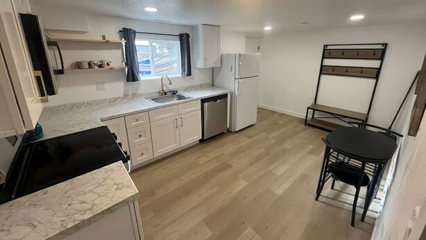 Una cocina compacta con armarios blancos, encimera negra y suelo de madera.