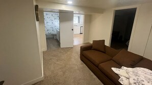 Una sala de estar con un sofá marrón, una manta blanca y una puerta que da a una cocina.