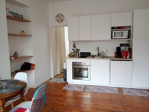 Une cuisine compacte avec des meubles blancs, un four à micro-ondes, un four traditionnel et une machine à café.