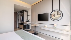 A modern hotel room with a bed, a small round table, a TV mounted on the wall, a mirror, and a vanity with a sink. - Foxtrail Sector 60- AM Hotel Kollection (Sohna)