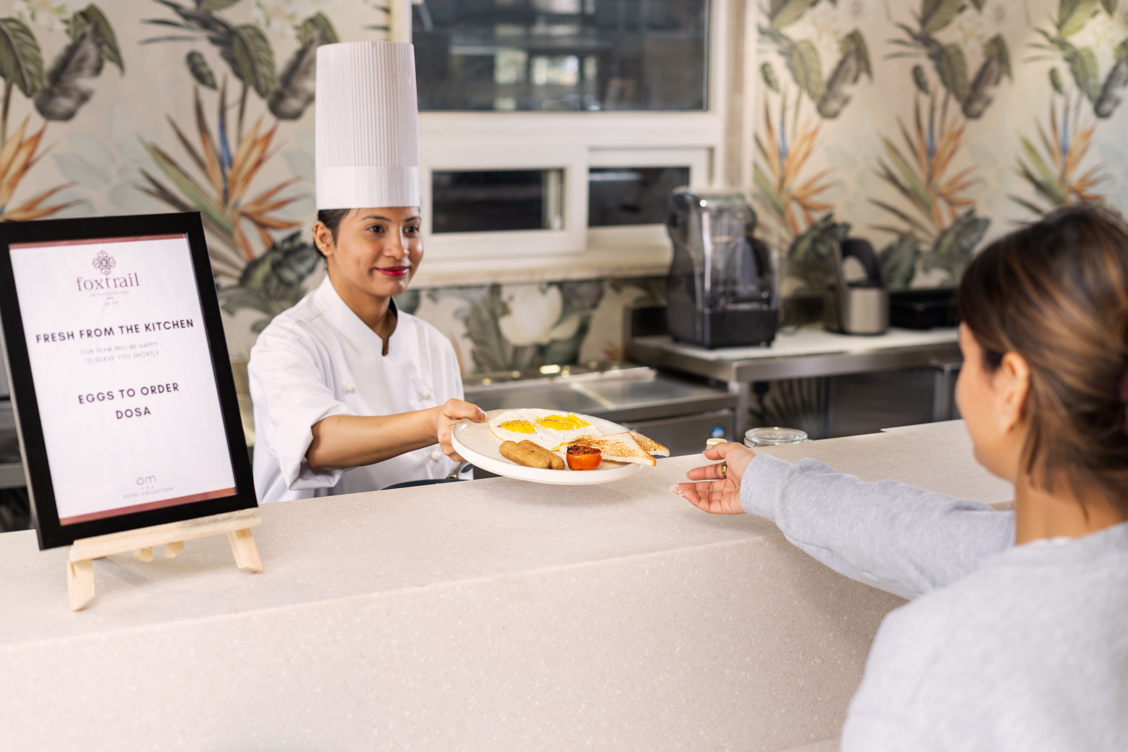 A person in a chef's uniform serving a plate of food to a customer at a counter.