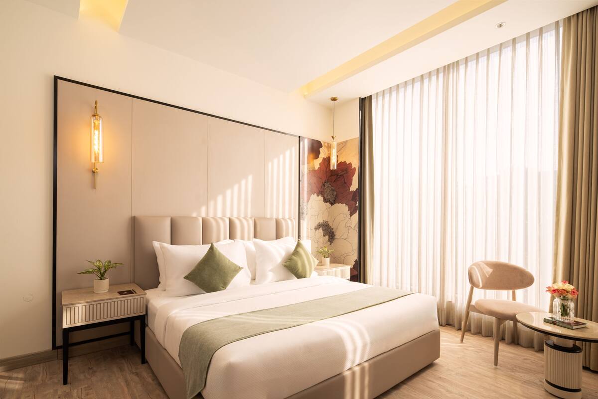 Une chambre d’hôtel moderne avec un grand lit, une table de chevet agrémentée d’une plante, une chaise et une petite table sur laquelle est posé un vase de fleurs.