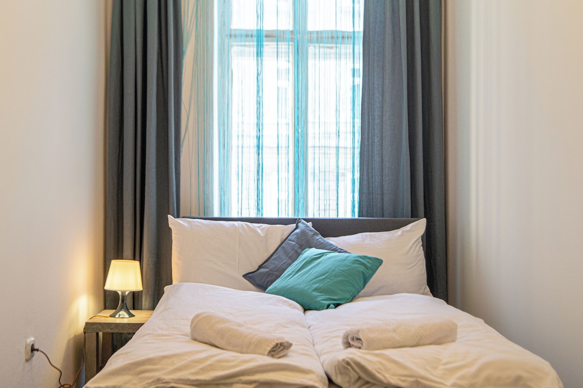 A neatly made bed with two pillows, a bedside lamp, and a window with curtains.