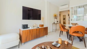 Un soggiorno moderno con una TV a schermo piatto, un mobile porta TV in legno, poltrone arancioni e una zona pranzo con tavolo in vetro.