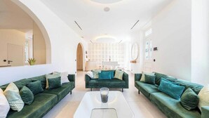 Ein modernes Wohnzimmer mit grünen Sofas, einem zentralen Couchtisch und einer weißen Wand mit Rastermuster.
