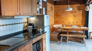 A kitchen with wooden cabinets, a countertop, a stove, a refrigerator, a dining table with benches, and a hanging light fixture. - 1BDR/4P apartment with balcony and parking- Megève (Megève)