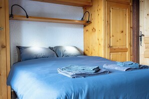 Ein Bett mit blauer Bettwäsche und zwei gefalteten Handtüchern, Holzwände und eine Tür mit einem Metallgriff.