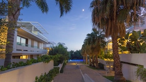 A modern hotel with a glass facade, a staircase leading to the entrance, and a well-maintained garden with palm trees. - Studio in Scoglitti, Sizilien (MARINA DI RAGUSA (RAGUSA))
