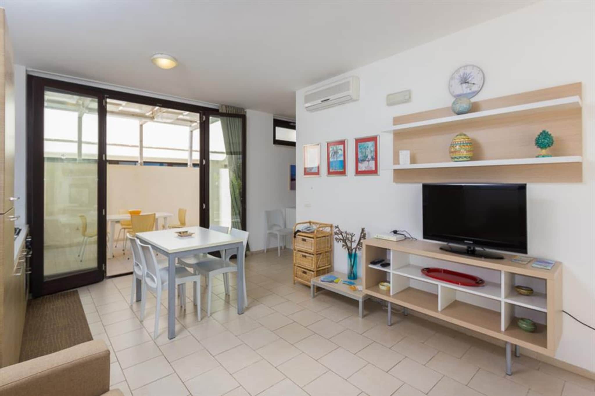 A modern living room with a dining area, a television, and a balcony with glass doors.