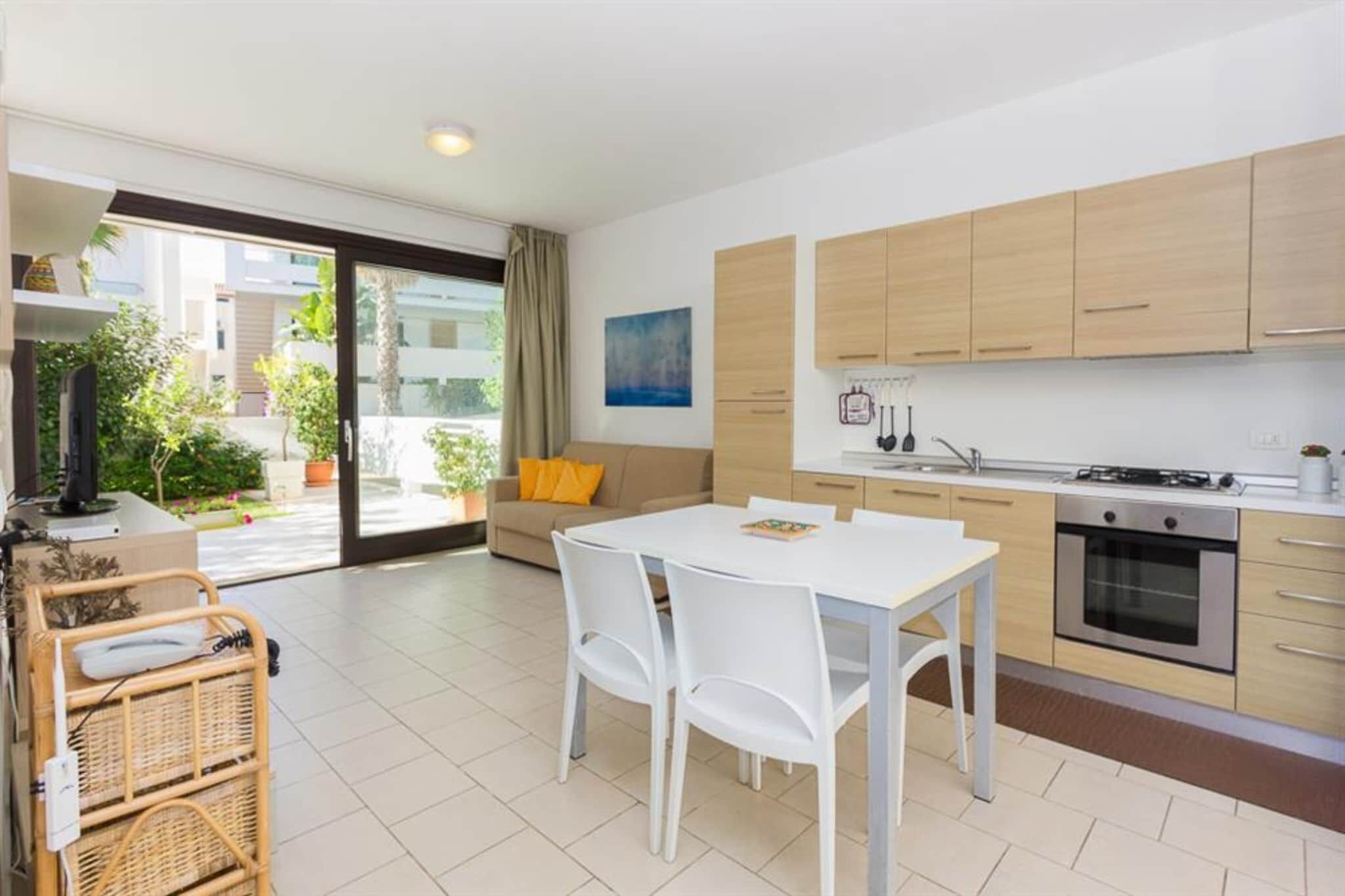 Eine moderne Küche mit weißen Schränken, einem Esstisch mit Stühlen und Blick auf einen Balkon mit Pflanzen.