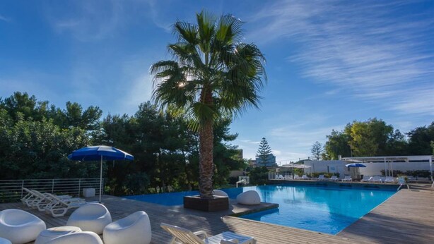 A pool area with lounge chairs, a palm tree, and a clear blue sky. - Studio in Scoglitti, Sizilien (MARINA DI RAGUSA (RAGUSA))