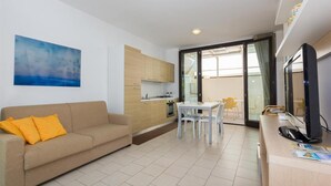 A modern living room with a sofa, a dining table, and a kitchen area. - Studio in Scoglitti, Sizilien (MARINA DI RAGUSA (RAGUSA))