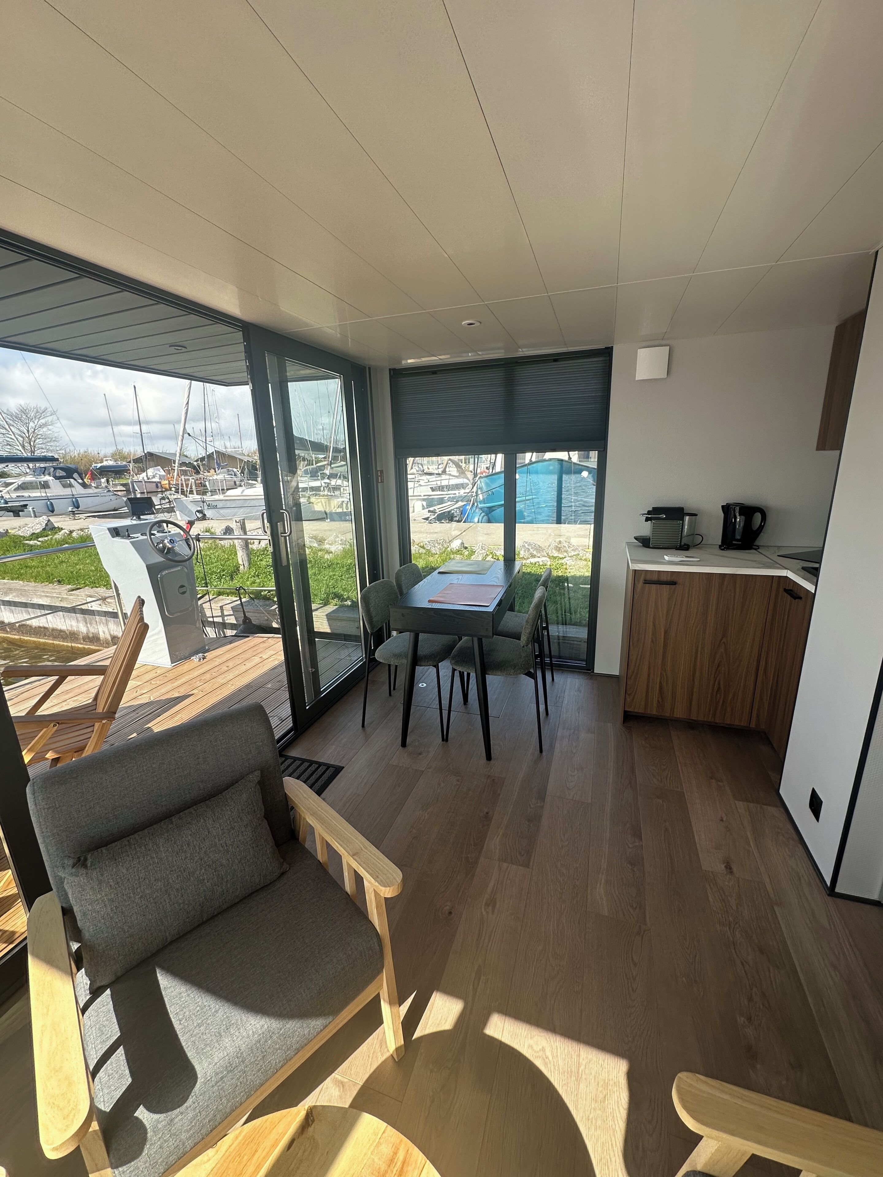 Een modern interieur met een eethoek, keuken en grote ramen met uitzicht op een jachthaven.