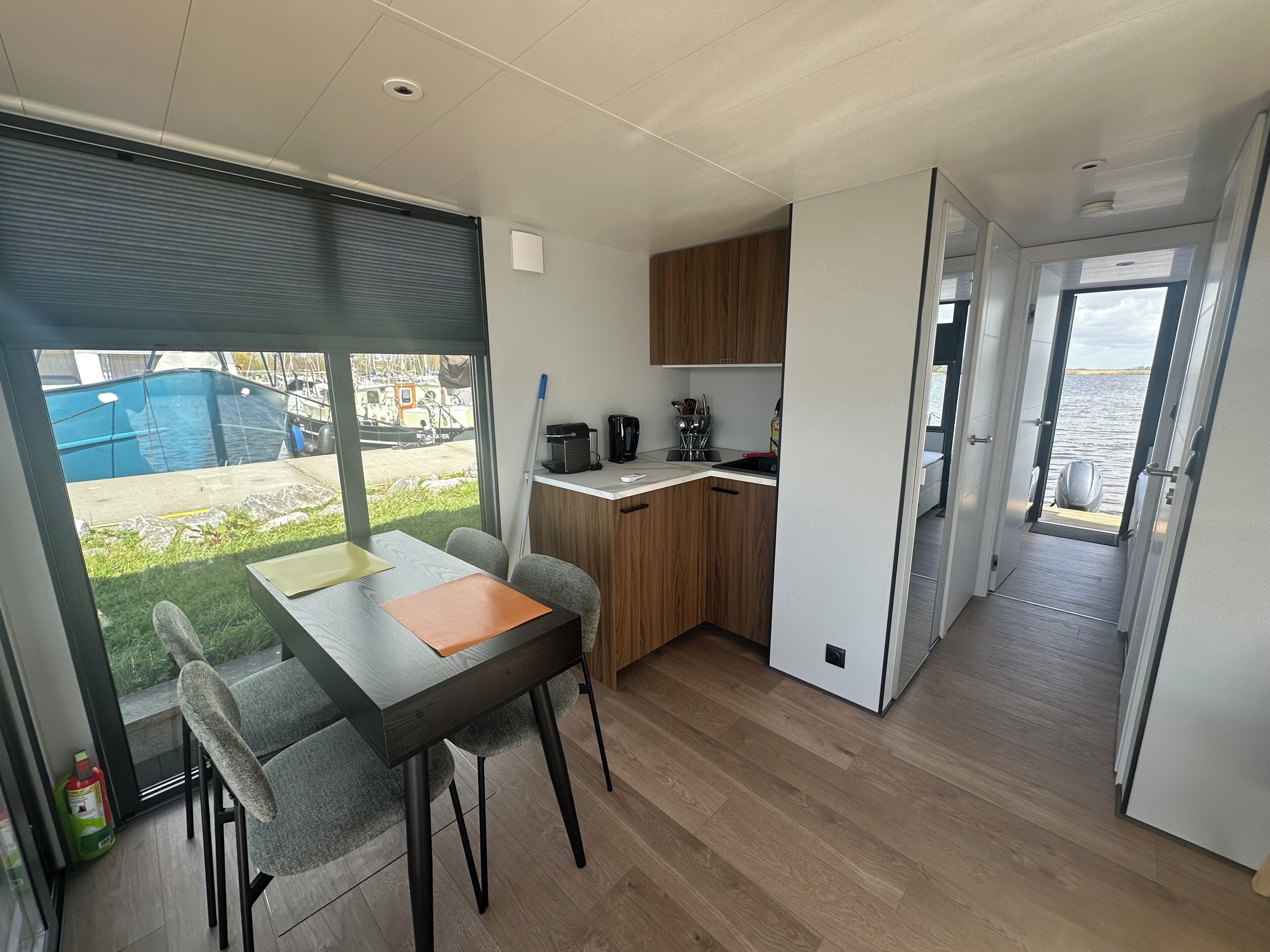 A modern kitchen with wooden cabinets, a dining area with a table and chairs, and a view of the outdoors through large windows.