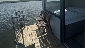 A deck with a bed and two chairs, overlooking a body of water. - Super nice houseboat with fantastic views! (Molkwerum)