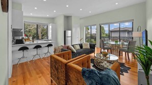 A spacious living area with a sofa, coffee table, and bar stools. A kitchen with a refrigerator and stove is visible in the background. - Luxurious 3-bedroom Townhouse in Charming Maidstone 7 KM TO CBD (Melbourne)