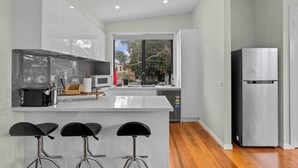 A modern kitchen with a central island, bar stools, a stainless steel refrigerator, and a view through large windows. - Luxurious 3-bedroom Townhouse in Charming Maidstone 7 KM TO CBD (Melbourne)