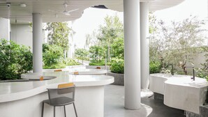 A modern outdoor seating area with white tables and chairs, surrounded by greenery and a view of the sky. - 22 Macalisterz by Mana Mana (George Town)