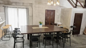 A conference room with a long wooden table, black chairs, a potted plant, and hanging pendant lights. - Capital O Dream Nur Private Pool Villa (Malacca City)