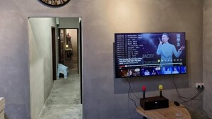 A room with a wall-mounted television displaying a music video, a clock, and a small speaker. - Capital O Dream Nur Private Pool Villa (Malacca City)