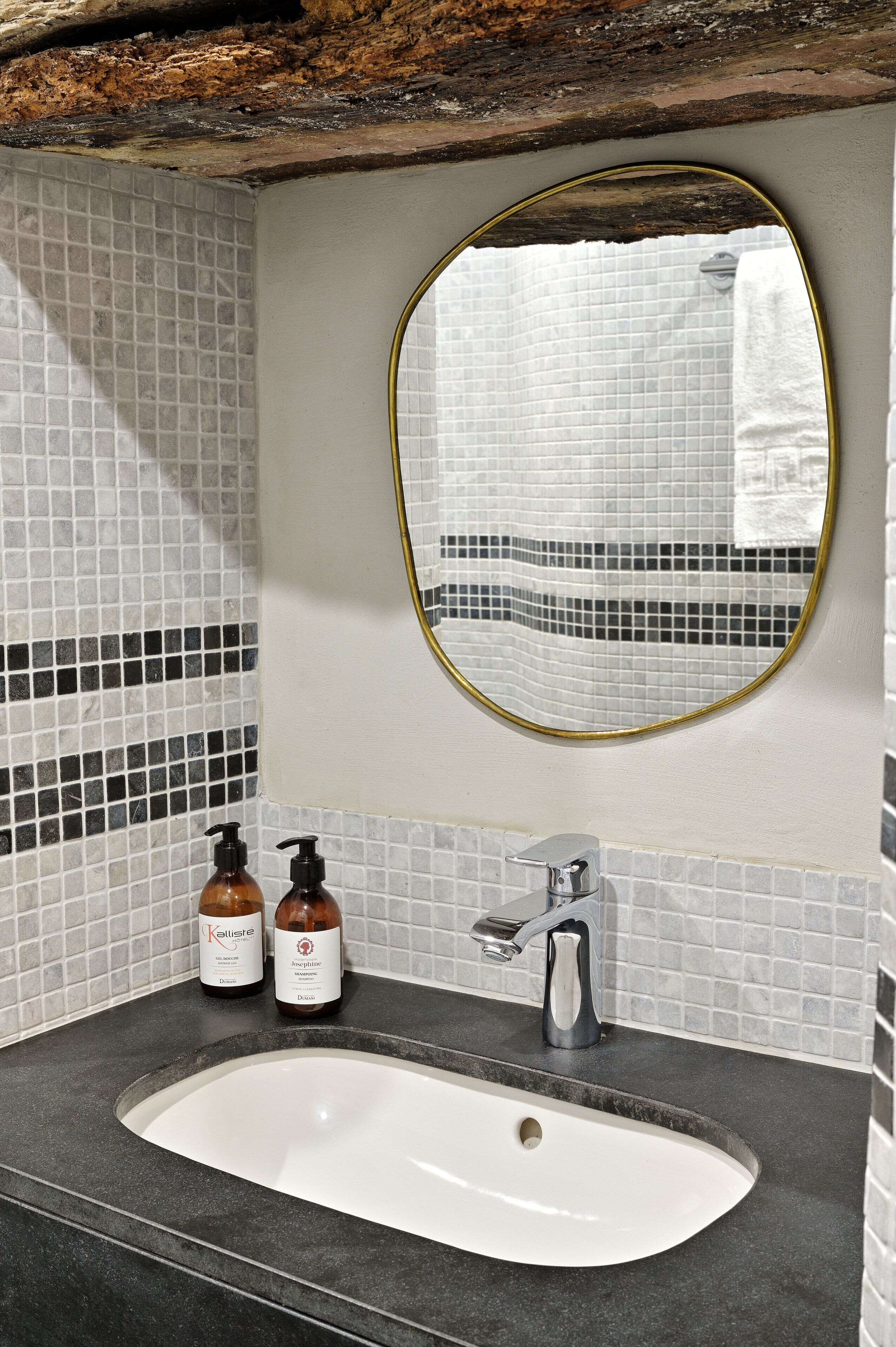Un bagno con un lavandino bianco, due erogatori di sapone, uno specchio e una parete rivestita di piastrelle.