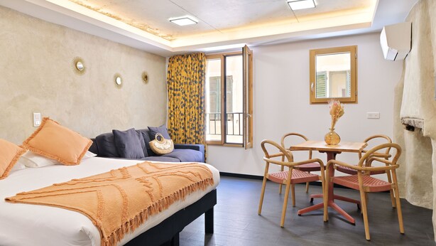 A hotel room with a bed, a dining table with chairs, a window with curtains, and a wall-mounted air conditioner.