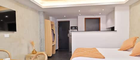 A modern hotel room with a bed, a desk with a cup, a chair, a wardrobe, and a kitchenette.