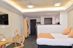 Ein modernes Hotelzimmer mit einem Bett, einem Schreibtisch mit Tasse, einem Sessel, einem Kleiderschrank und einer Küchenzeile.