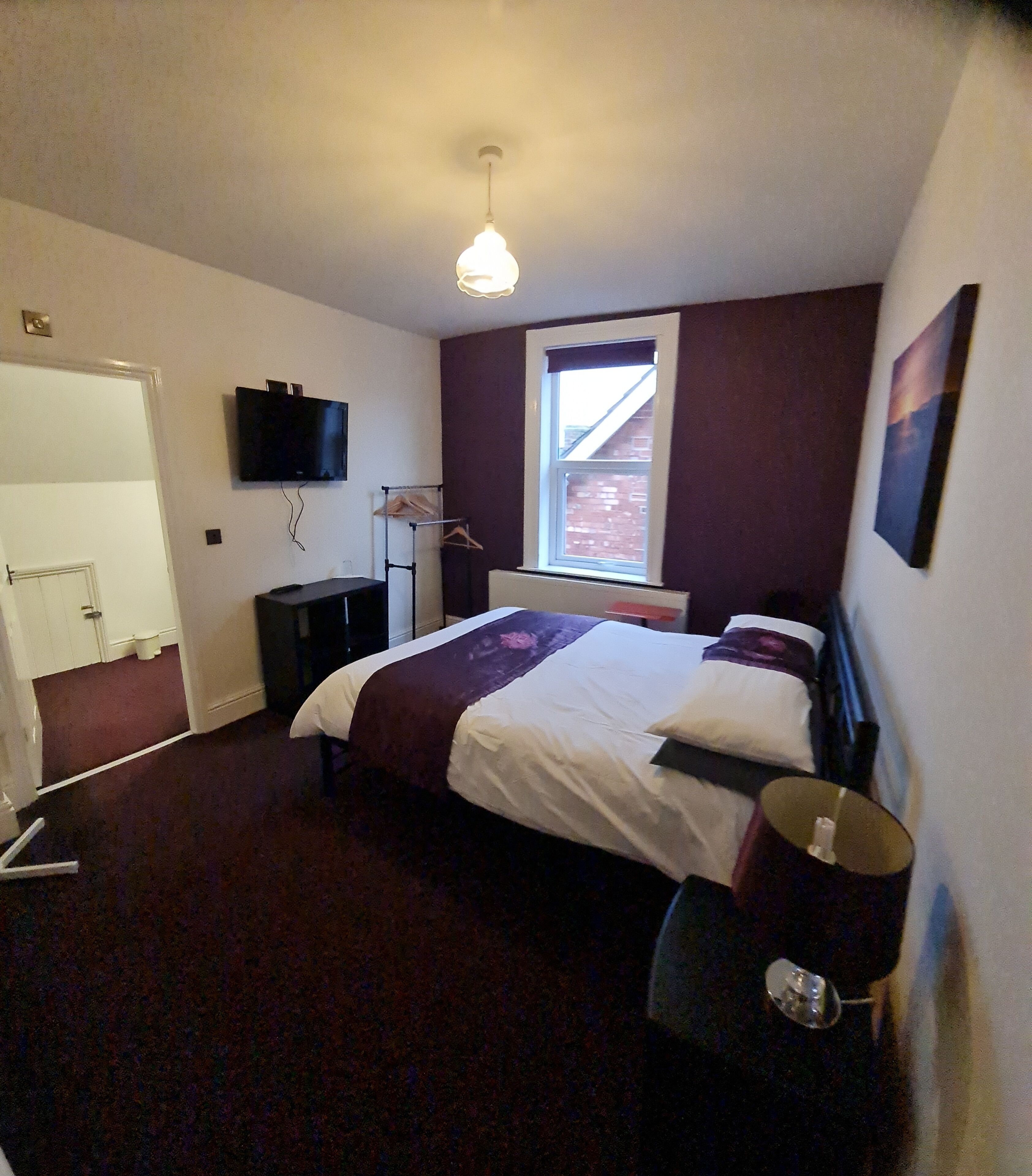 A bedroom with a bed, bedside table, lamp, and a window.