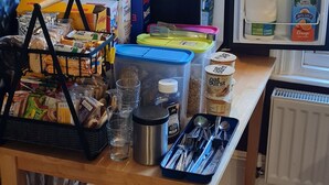 A kitchen area with a refrigerator, microwave, and a wooden table with various food items and kitchenware. - Crittlewood Guest House (Gainsborough)