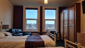 A hotel room with a bed, a desk, a chair, a wardrobe, and two windows with a view of buildings outside. - Crittlewood Guest House (Gainsborough)