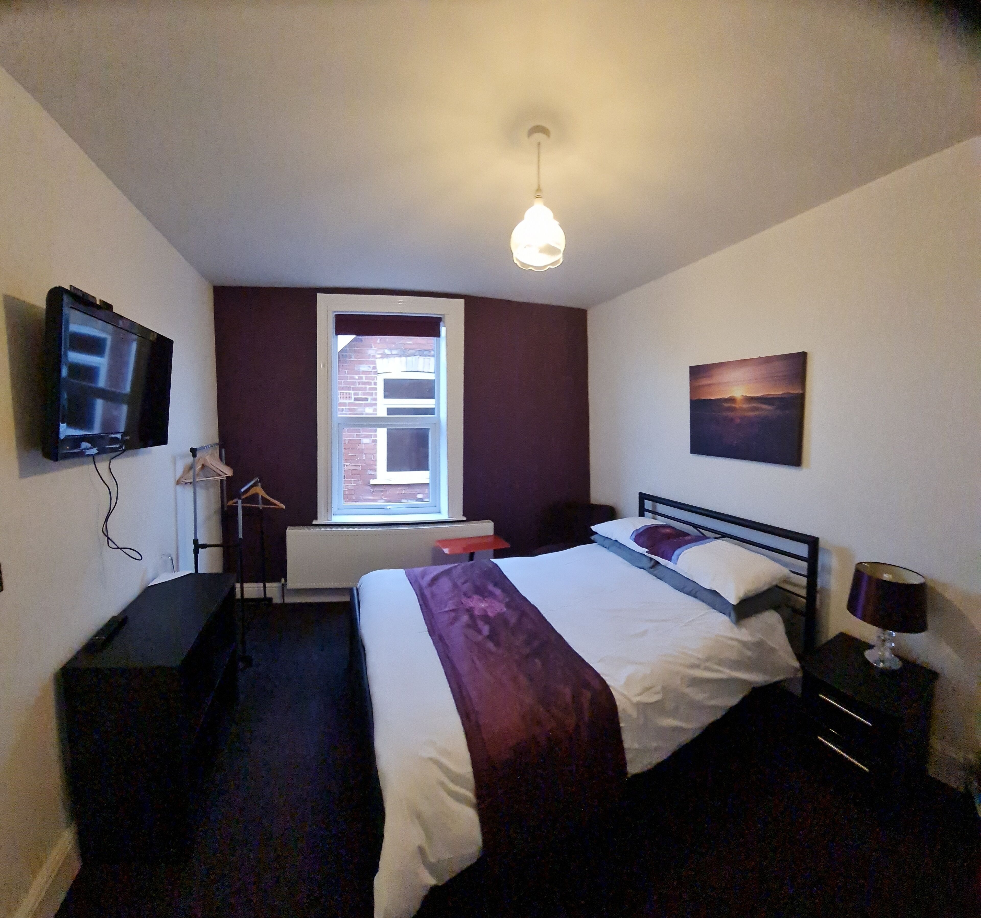 Habitación de hotel con cama, televisión, ventana, un cuadro y escritorio.